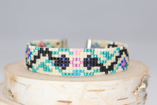 Load image into Gallery viewer, black and silver snakes on a cream background with green vines and blue, turquoise, pink and yellow flowers. made of premium Delica seed beads. handmade bracelet