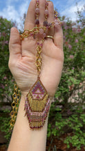 Load and play video in Gallery viewer, Boho long beaded necklace with a hint of southwest spice featuring a gorgeous hand beaded seed bead fringed pendant in shades of pink, purple, mauve, gold & burgundy.  the pendant has tiny garnets at the ends of the fringe along the bottom of the pendant. The necklace consists of chunky brass chain accented with natural round & star cut strawberry quartz, and faceted pink tourmaline cubes.  38 inches long. could be shortened upon request.