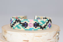 Load image into Gallery viewer, black and silver snakes on a cream background with green vines and blue, turquoise, pink and yellow flowers. made of premium Delica seed beads. handmade bracelet 
