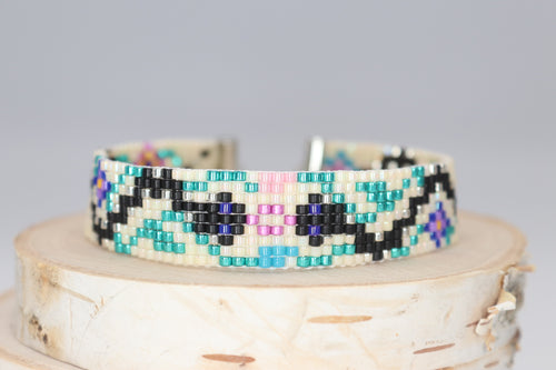 black and silver snakes on a cream background with green vines and blue, turquoise, pink and yellow flowers. made of premium Delica seed beads. handmade bracelet 