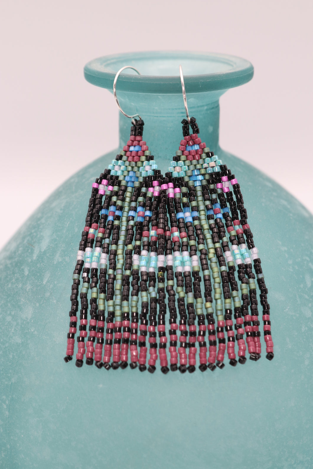 3 inch long by .75 inch wide seed bead fringe earrings. Handmade. Black base with plum, aqua, pink, and lavender floral pattern with green leaves and stems