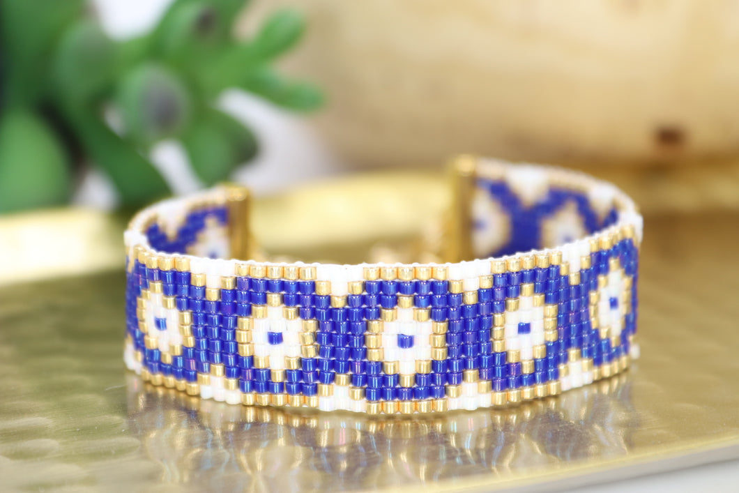 handmade seed bead bracelet in a cobalt blue, gold, and pearly white evil eye pattern. adjustable with a lobster claw and chain closure