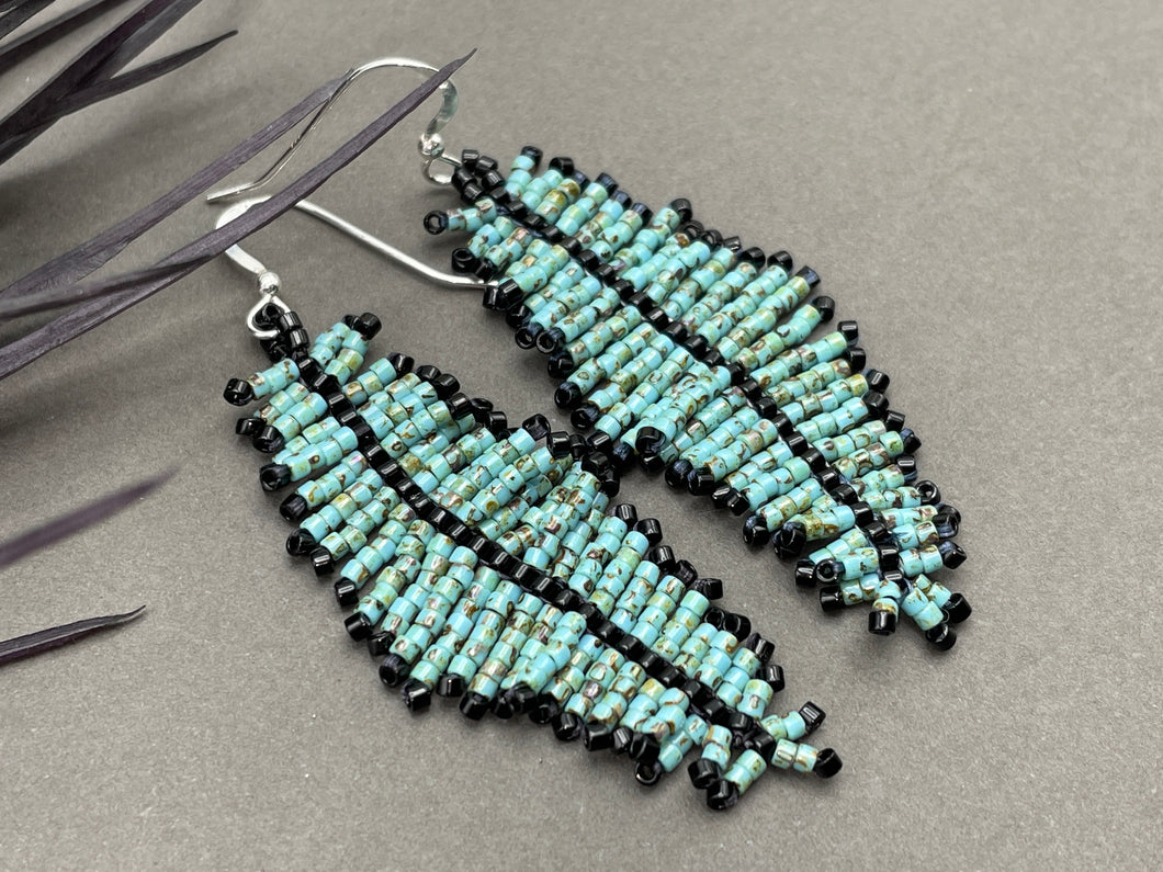 2.5 inch long seed bead beaded feather earrings in a turquoise green Picasso finish with black accents. hung on sterling silver ear wires